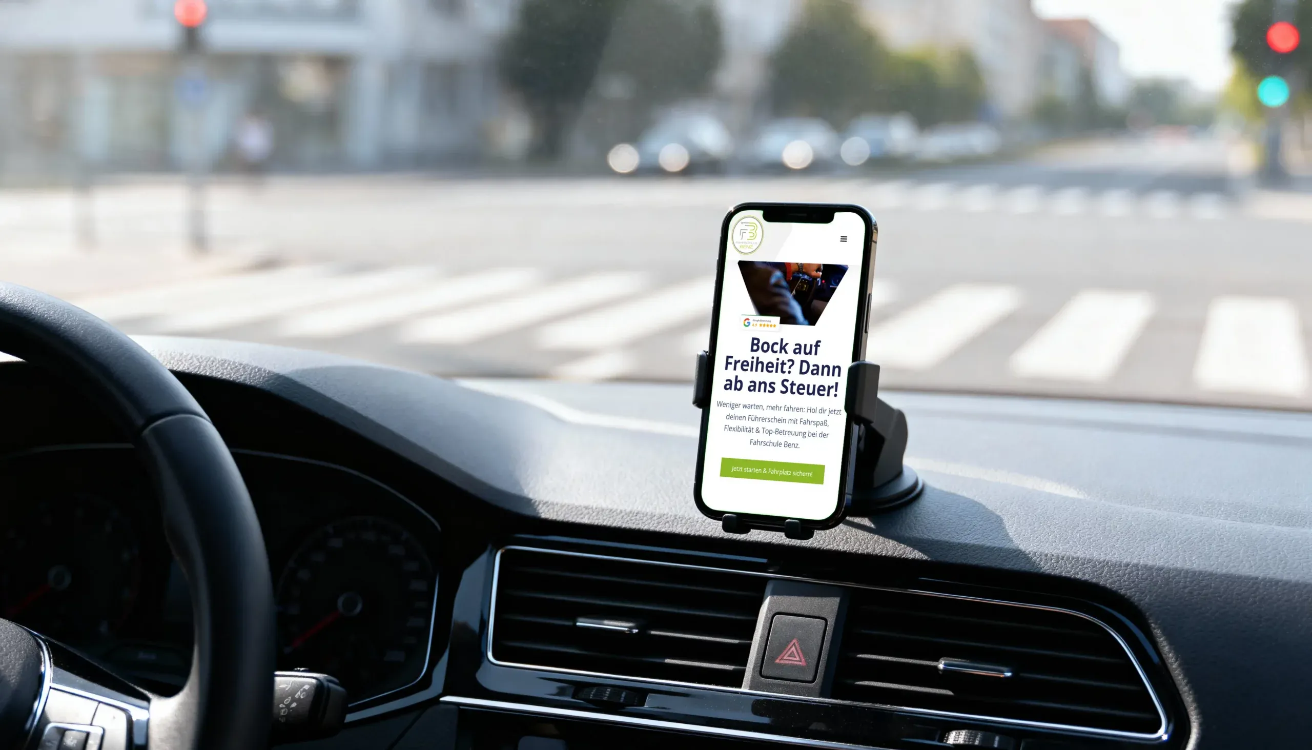Smartphone in einer Handyhalterung im Auto zeigt die Startseite von fahrschulebenz.com mit dem Slogan „Bock auf Freiheit? Dann ab ans Steuer!“