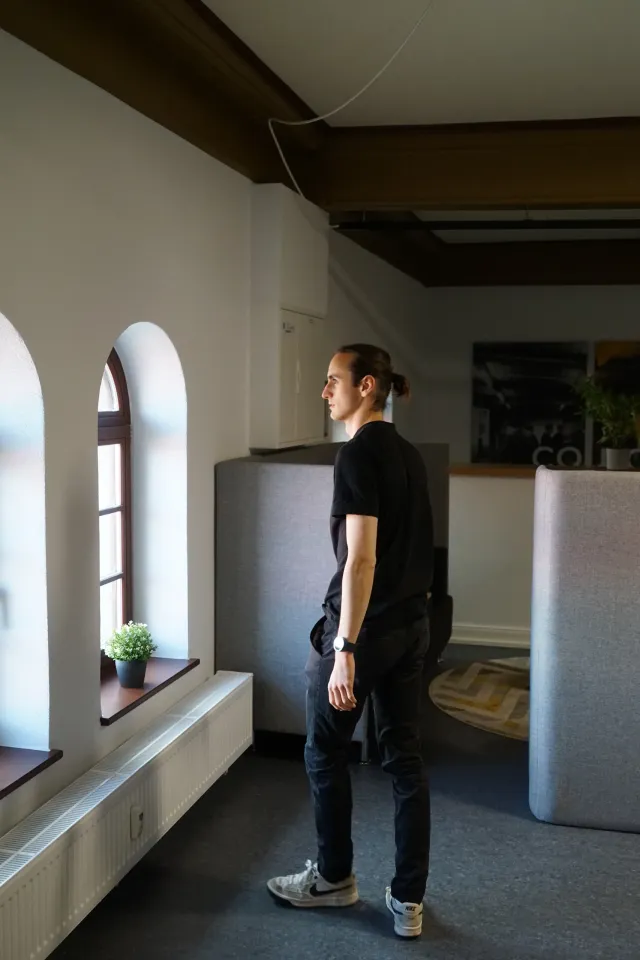 Mitarbeiter von GRZ Digital steht in einem Büro mit Rundbogenfenstern und Holzbalkendecke.