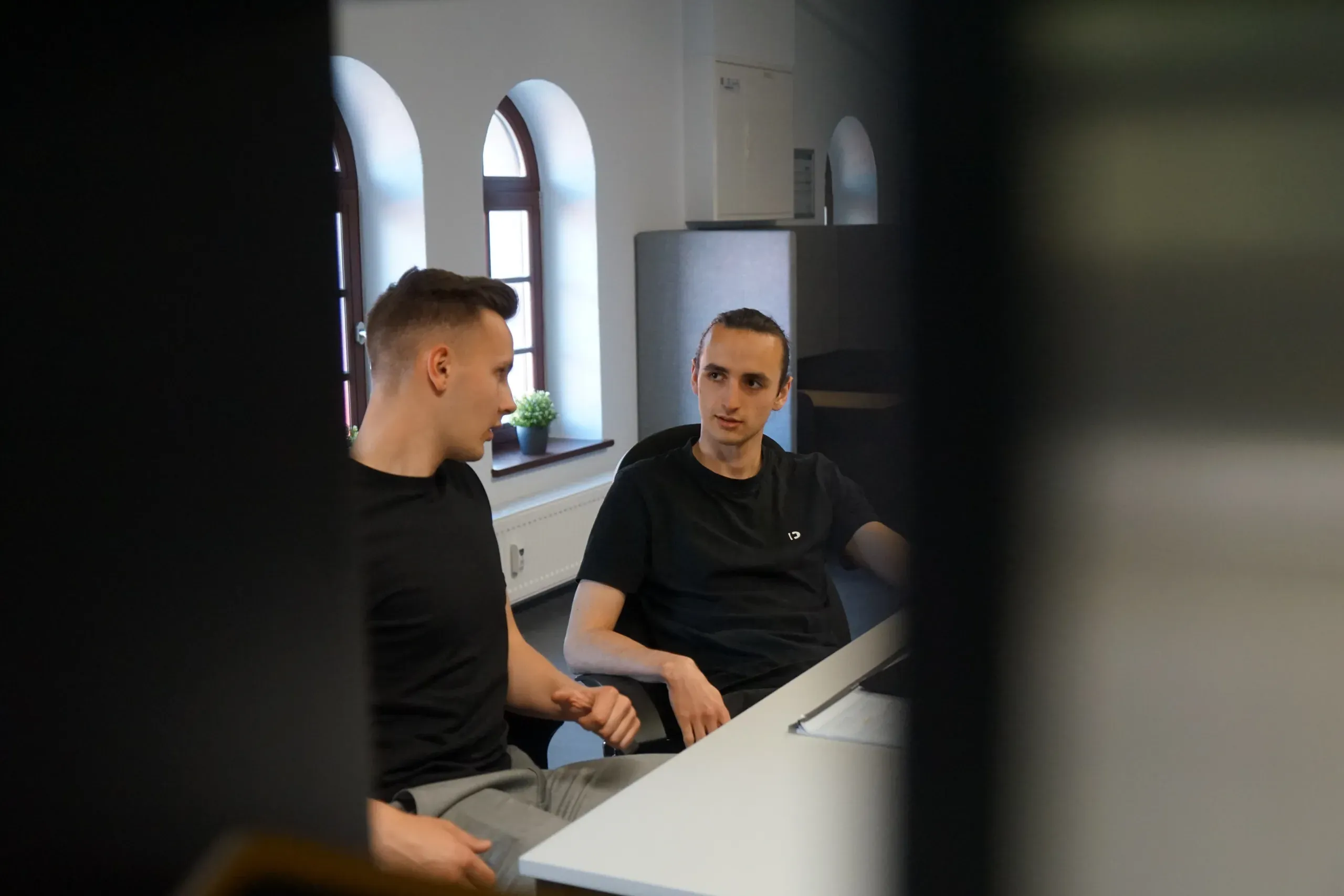 Zwei Mitarbeiter von GRZ Digital im Gespräch im Büro mit Rundbogenfenstern.