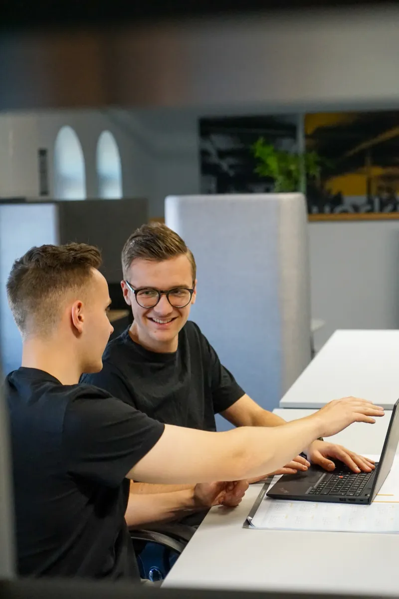 Zwei Mitarbeiter von GRZ Digital arbeiten gemeinsam an einem Laptop im Büro.