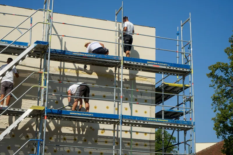 Vier Handwerker arbeiten auf einem Gerüst an einer Fassade mit frisch verlegten Dämmplatten.