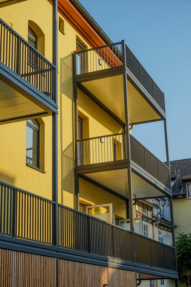 Saniertes Mehrfamilienhaus mit gelber Fassade und neuen Balkonen – Referenzobjekt der Richardt GmbH.