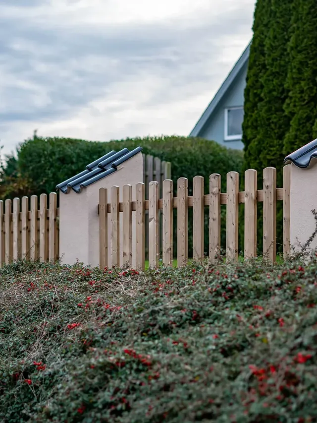 Vorgartenzaun aus Thermoholz zwischen gemauerten Pfosten.