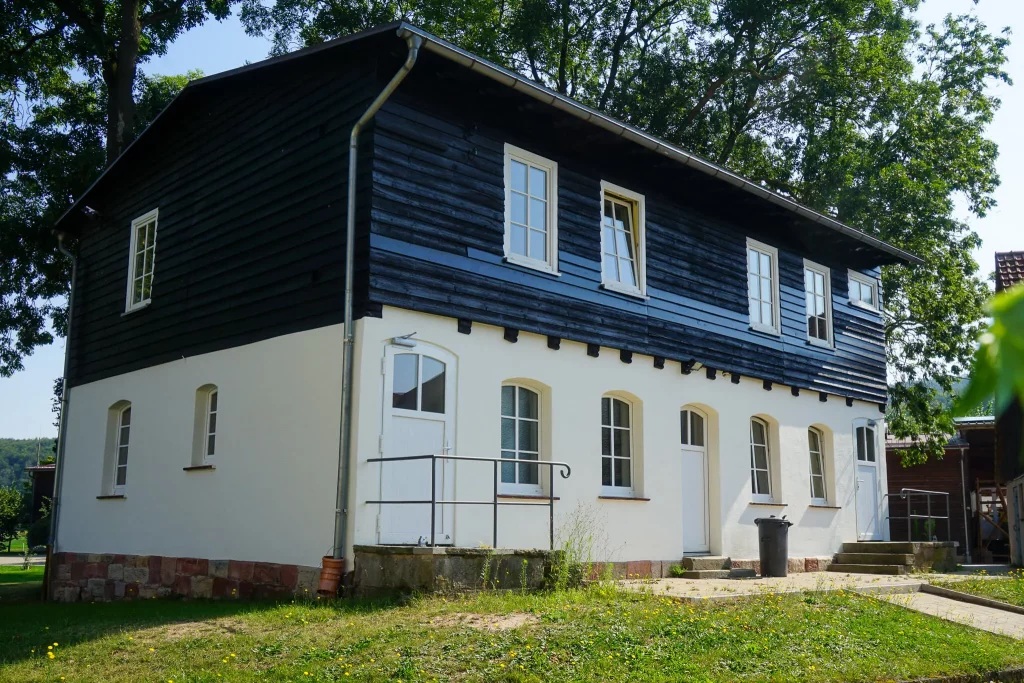 Referenz richardt.com, Modernisierte Hausfassade mit weißem Putz und dunklem Holzschindel-Obergeschoss, umgeben von Bäumen.